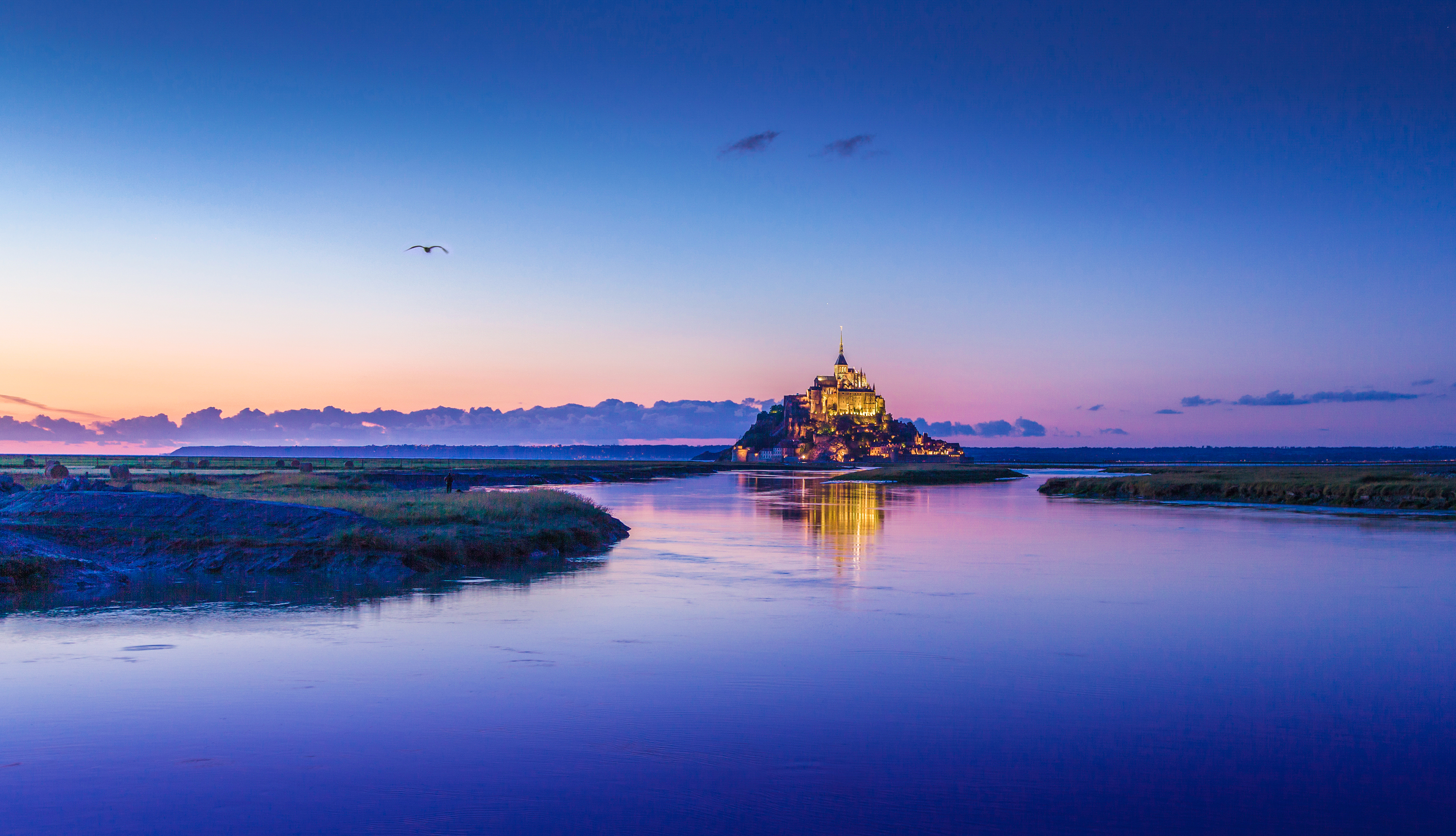 Der Mont-Saint-Michel in der Normandie bei Sonnenuntergang, malerisch auf einer Felseninsel im Wattenmeer gelegen und von warmem Abendlicht angestrahlt.