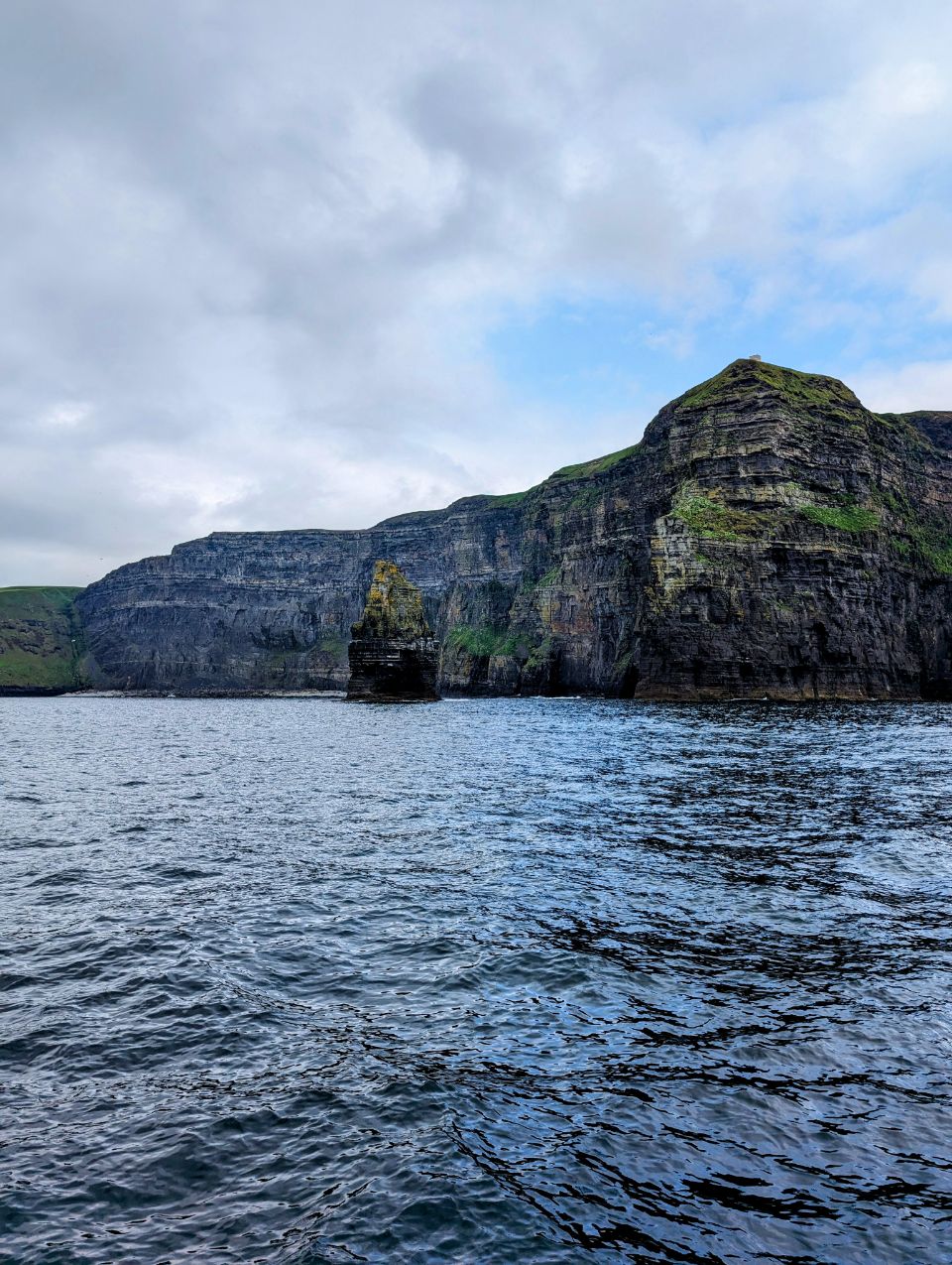 Vom Meer aus bietet sich hier ein majestätischer Blick auf die Cliffs of Moher in Irland. Die Perspektive vom Boot aus verdeutlicht die immense Höhe der Klippen, vor denen der berühmte Brandungspfeiler „Branaunmore“ aus dem Wasser ragt.