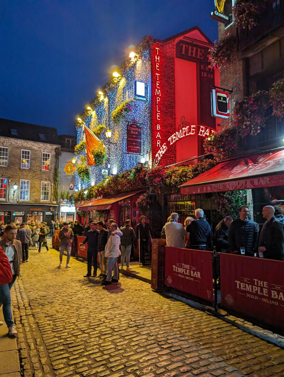 Das pulsierende Nachtleben Dublins wird in diesem Bild vor dem berühmten „The Temple Bar“ Pub eingefangen. Zahlreiche Menschen beleben die kopfsteingepflasterte Gasse, während der üppig mit Lichterketten geschmückte, rote Pub eine unglaublich einladende und lebendige Atmosphäre ausstrahlt.