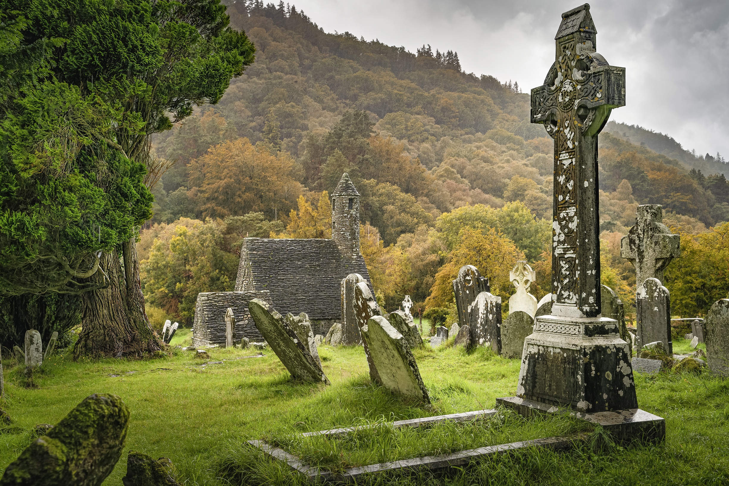 Historische Klosterruine Glendalough in Irland mit keltischen Hochkreuzen, alten Grabsteinen und herbstlich gefärbtem Wald – beliebte Sehenswürdigkeit in den Wicklow Mountains.
