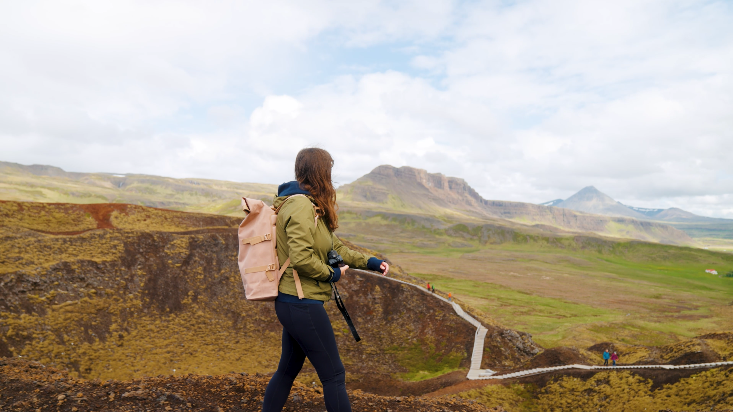 Auf diesem Bild überblickt eine Wanderin von der Kante des Kerið-Kraters in Island die beeindruckende Vulkanlandschaft. Die Aufnahme fängt die Weite der Umgebung und die einzigartige geologische Formation dieses berühmten Kraters am Golden Circle ein.