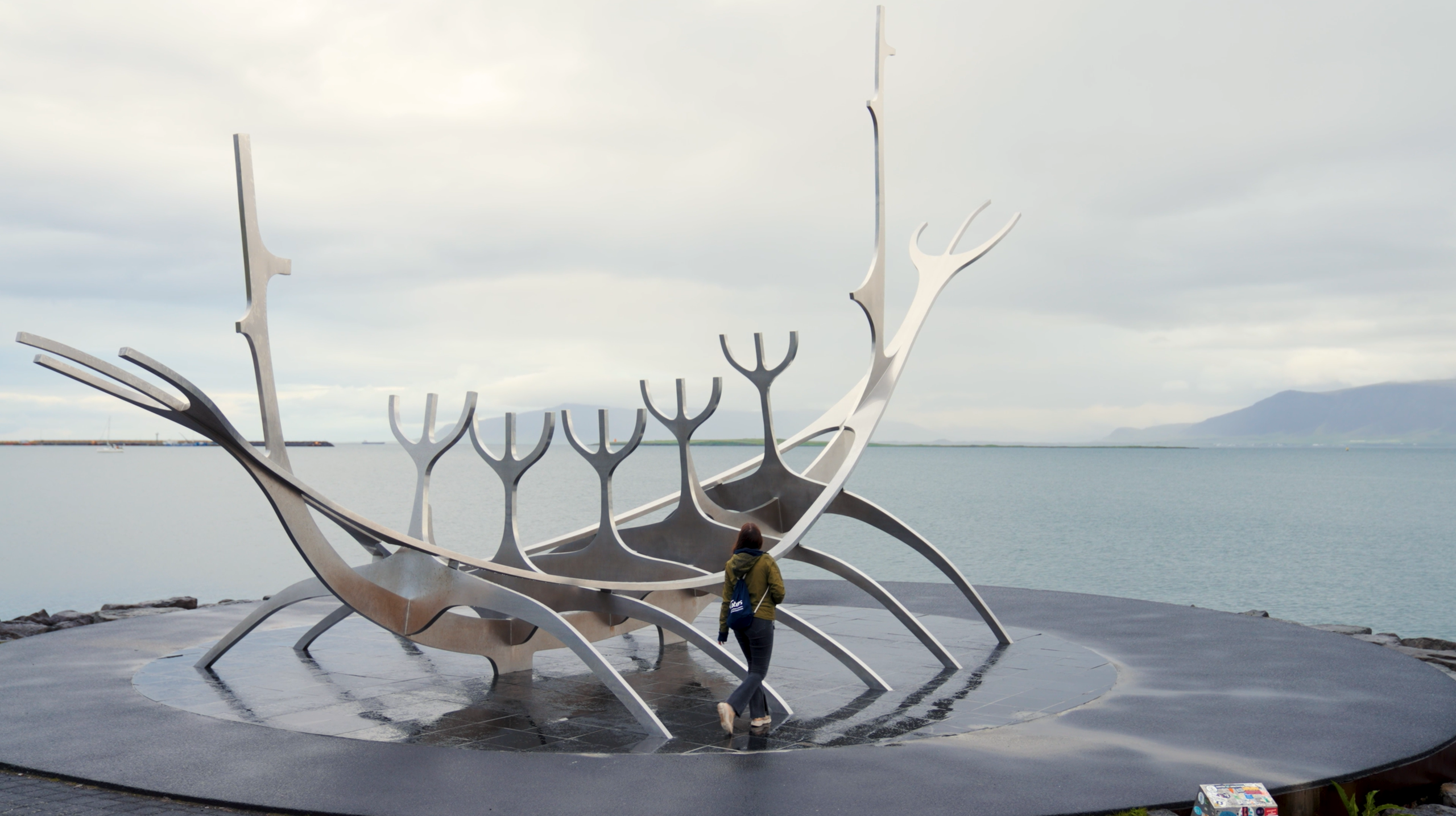 An der Uferpromenade von Reykjavík in Island ist eine Frau zu sehen, wie sie die berühmte Skulptur „Sólfar“ (Sonnenfahrt) umrundet. Das stilisierte Wikingerschiff aus Edelstahl ist eines der bekanntesten Wahrzeichen der Stadt und symbolisiert die Entdeckergeschichte Islands vor der Kulisse des Meeres.