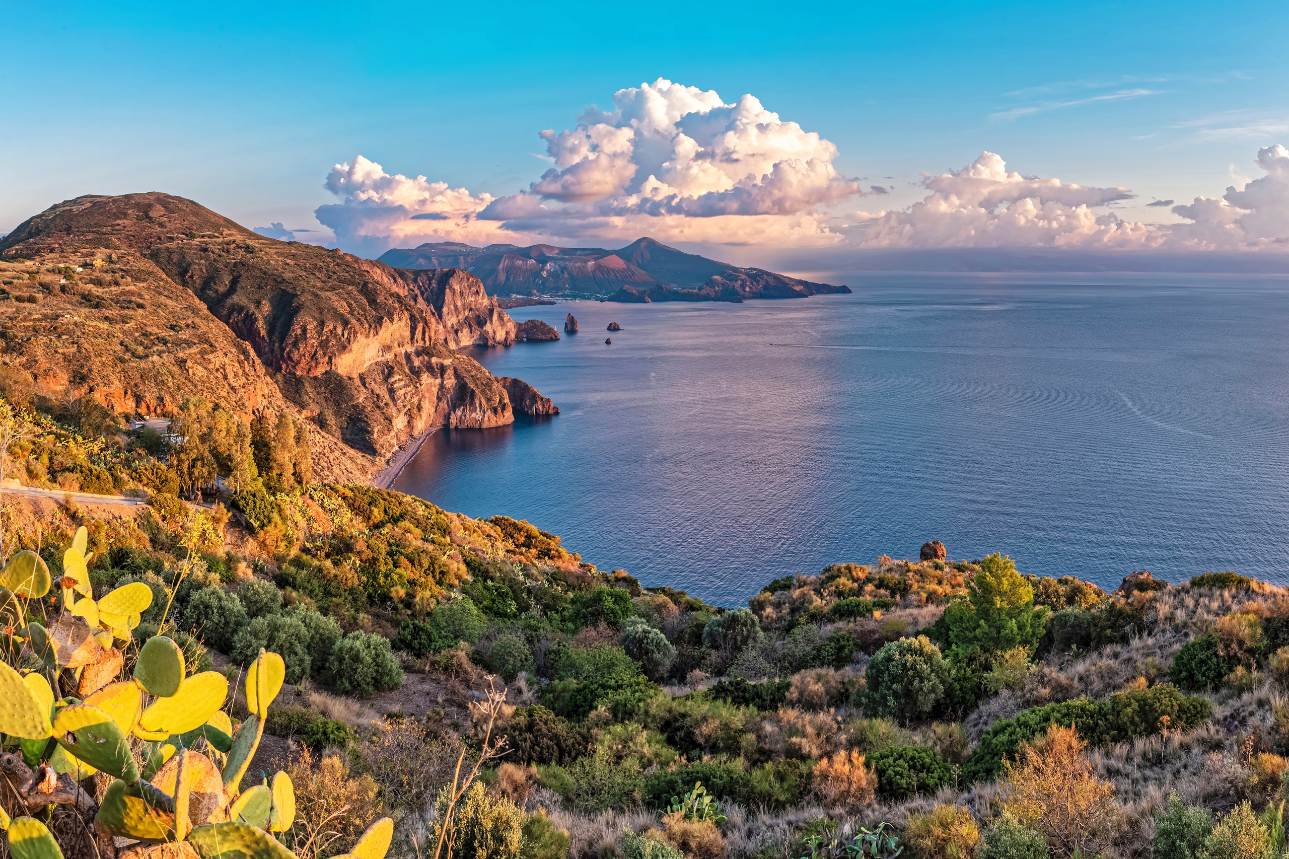 Blick auf die Küste von Lipari, eine der Äolischen Inseln in Italien, mit roten Felsen, tiefblauem Meer und weiter Aussicht bis zu den Nachbarinseln.