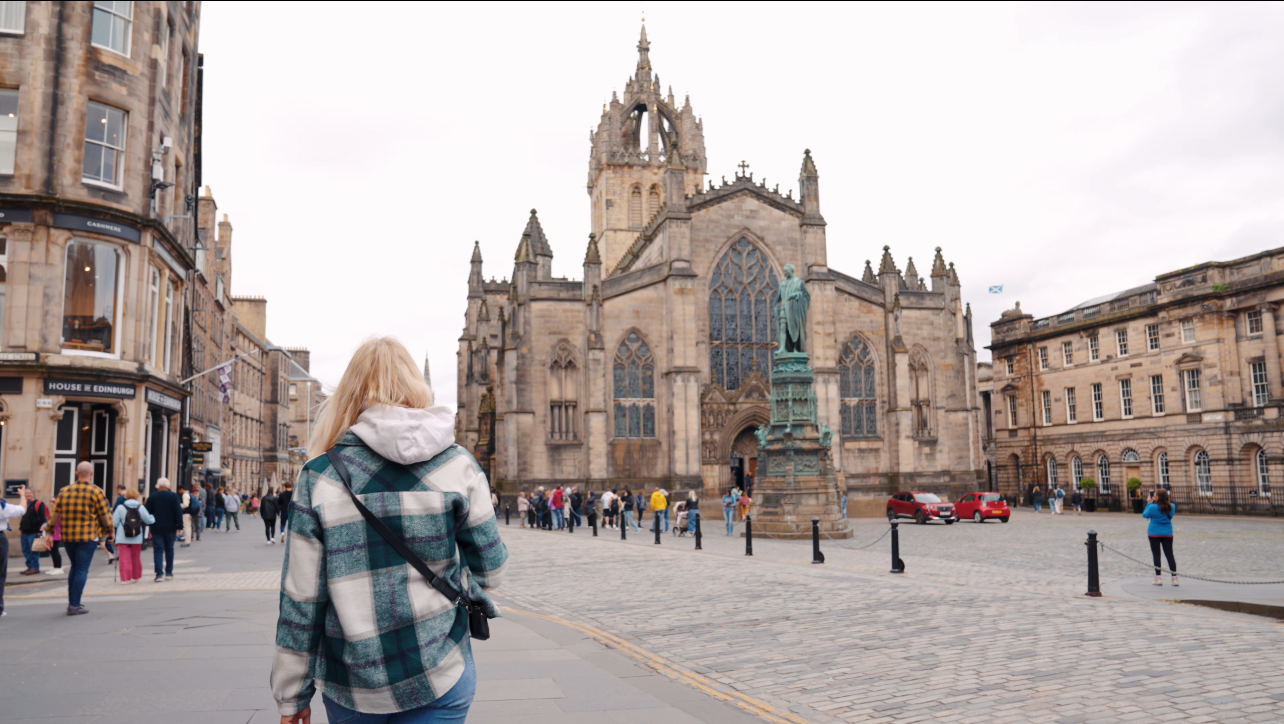 Eine Frau spaziert während eines Städtetrips in Edinburgh, Schottland, über den belebten Platz vor der imposanten St. Giles' Cathedral und bewundert die historische gotische Architektur dieser bedeutenden kulturellen Sehenswürdigkeit.