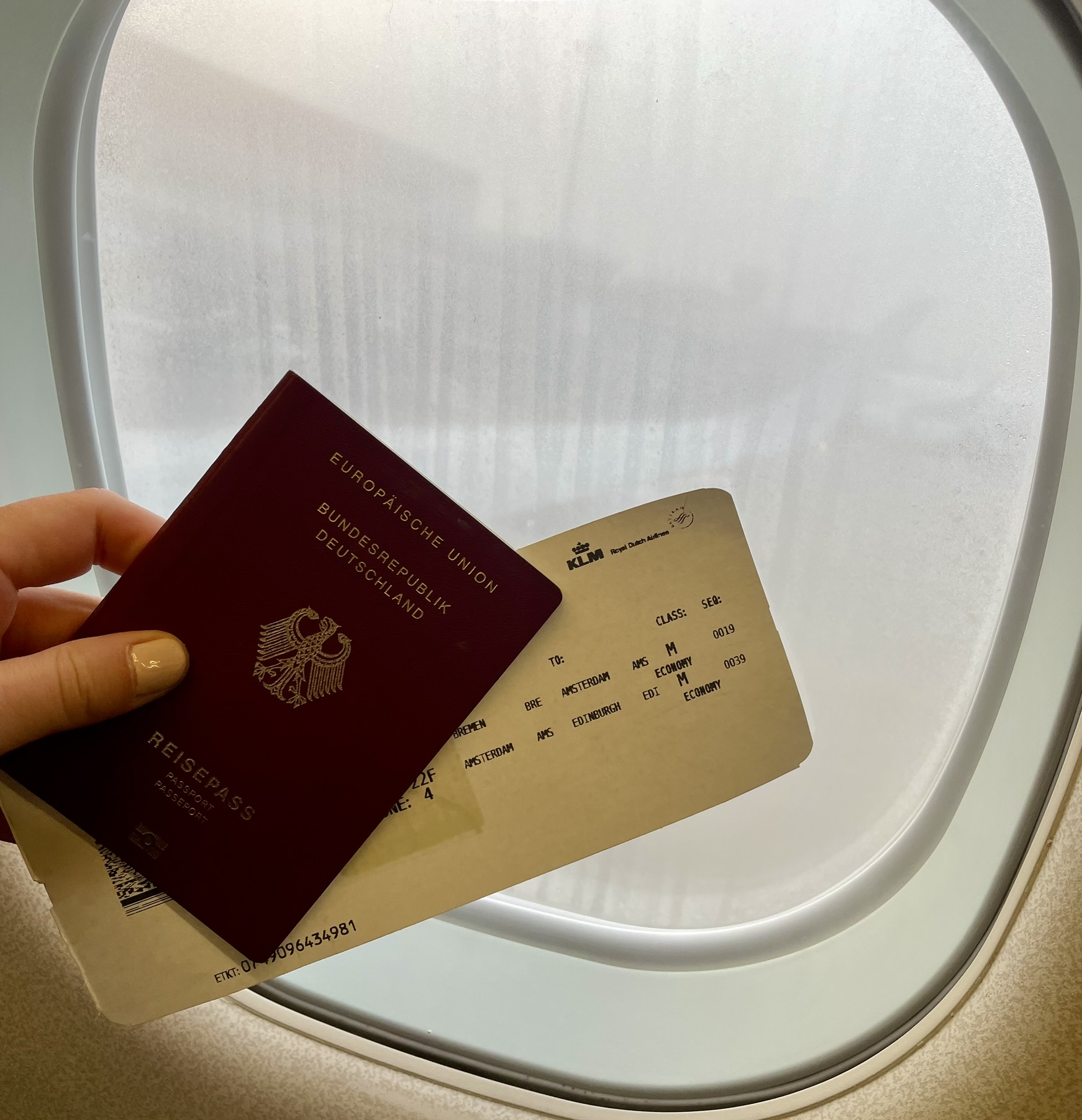 Eine Hand hält einen deutschen Reisepass und eine Bordkarte vor ein Flugzeugfenster und symbolisiert so den aufregenden Start in eine Flugreise zu einem neuen Urlaubs-Abenteuer.