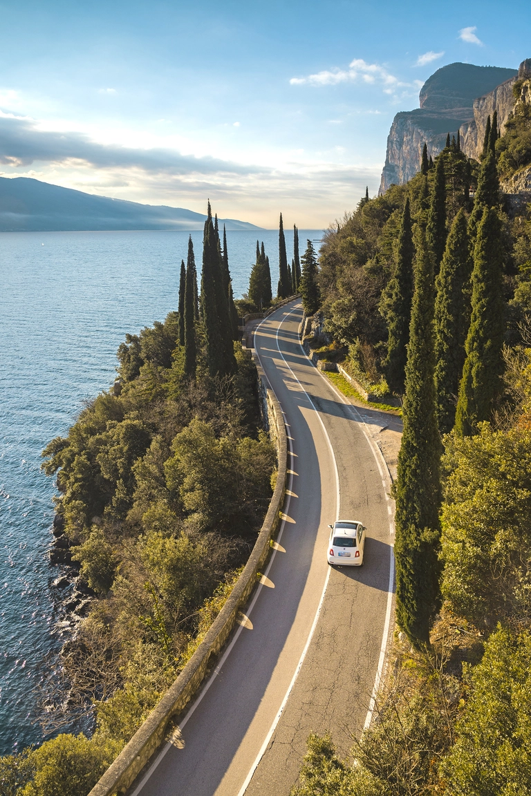 Auto fährt auf einer Panoramastraße am Gardasee entlang, umgeben von Zypressen und Felsen – typisch für eine Italien-Rundreise mit dem Auto.