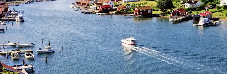Boohuslän - Schwedische Westküste mit rooten Bootshäusern Boot fährt durch einen Schärenkanal bei Bohuslän, umgeben von kleinen Inseln und typischen roten Holzhäusern. Sommerliches Küstenpanorama in Westschweden.